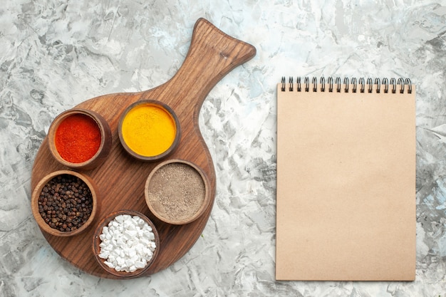 Top view of different spices on cutting board and notebook on white background