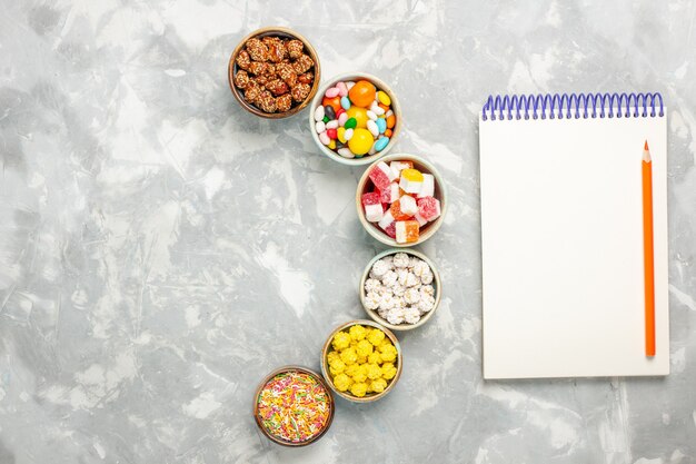 Free photo top view of different sweet candies with marshmallows and notepad on white surface