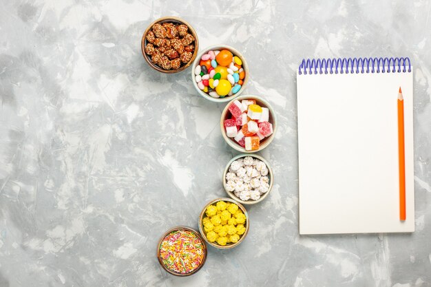 Вид сверху различных сладких конфет с зефиром и блокнотом на белой поверхности