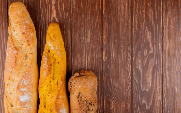 Top view of different types of baguette on wooden background with copy space