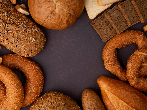 Top view of different types of bread as bagel classic and seeded cob rye and white bread slices baguette on maroon background with copy space