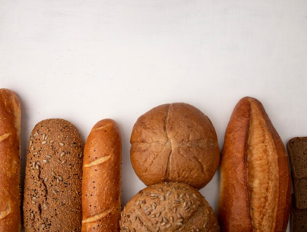 Top view of different types of bread as baguette cob rye on white background with copy space