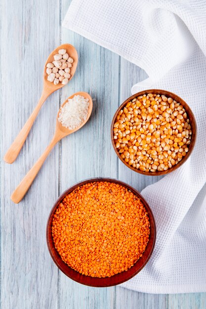 Top view of different types of groats and seeds in wooden bowls and spoons red lentils corn seeds rice and chickpeas