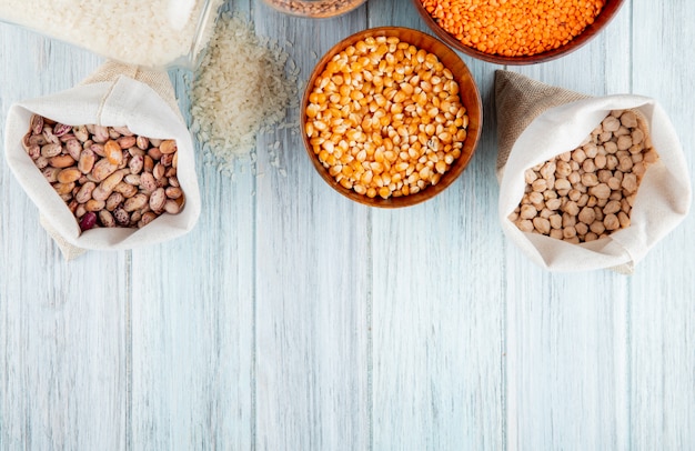 Top view of different types of legumes and cereals kidney beans rice dried corns red lentils and chickpeas in sacks and bowls on rustic background with copy space