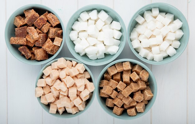 Top view of different types of lump sugar in bowls on white background