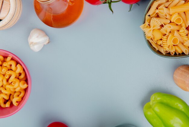 Top view of different types of pasta as cavatappi pipe-rigate and others with garlic butter pepper salt on blue surface with copy space