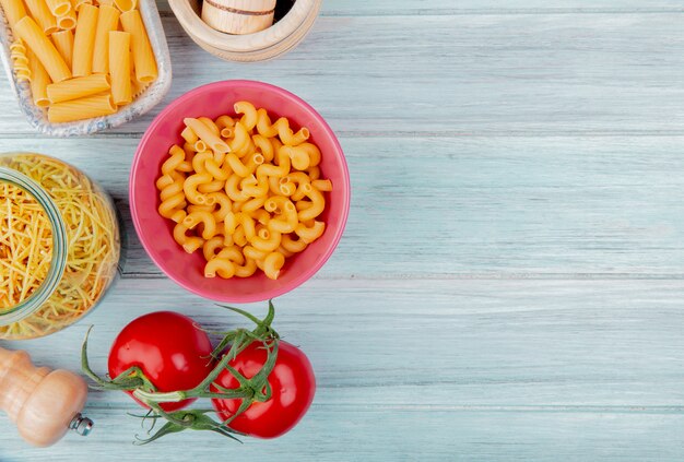 Top view of different types of pasta as cavatappi ziti spaghetti with tomato salt on wooden surface with copy space