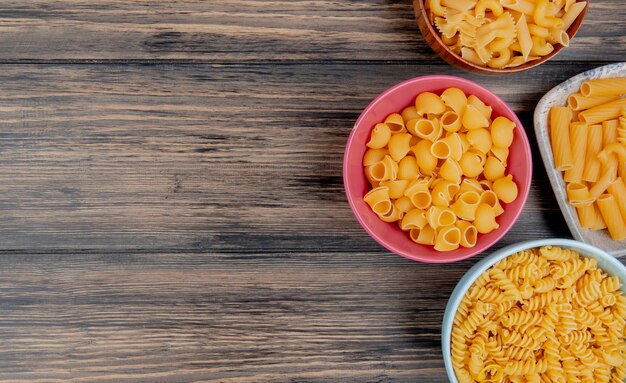 Top view of different types of pasta as pipe-rigate rotini ziti and others on wooden surface with copy space