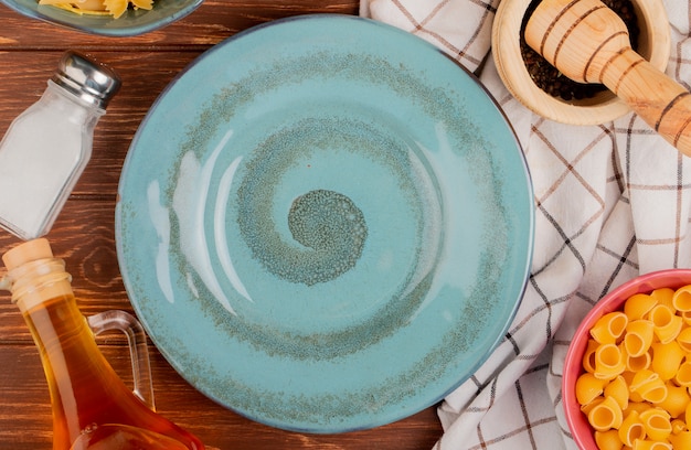 Free photo top view of different types of pasta in bowls salt black pepper butter around plate on wooden surface