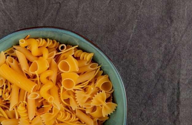 Top view of different types of pasta on gray cloth surface with copy space