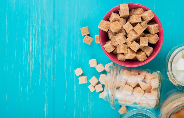 Free photo top view of different types of sugar in bowls and in glass jars on blue wooden background with copy space