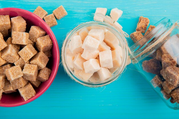 Top view of different types of sugar in glass jars on blue wooden background