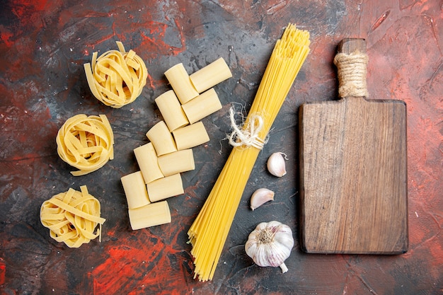 Foto gratuita vista dall'alto di diversi tipi di pasta cruda e tagliere di legno aglio su sfondo nero