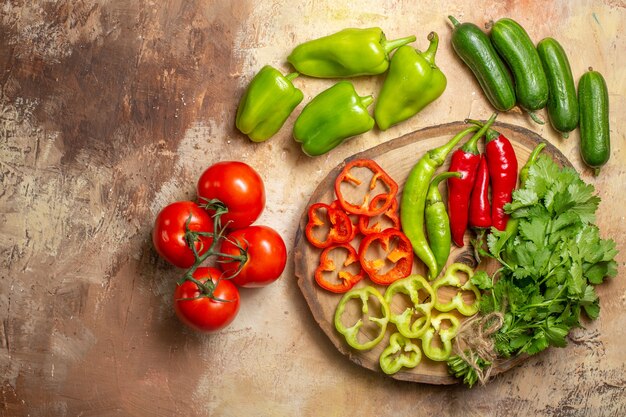 Top view different vegetables cut into pieces on round tree wood board tomatoes cucumbers on yellow ochre background