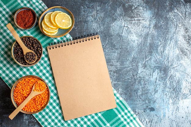 Top view of dinner background with different spices yellow pea and spiral notebook on dark table