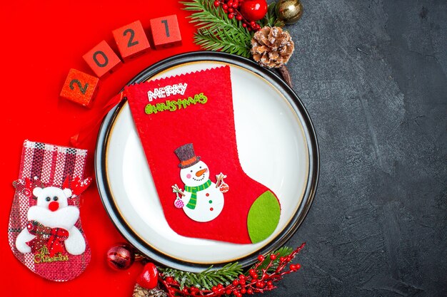 Top view of dinner plate decoration accessories fir branches and numbers christmas sock on a red napkin on a black background