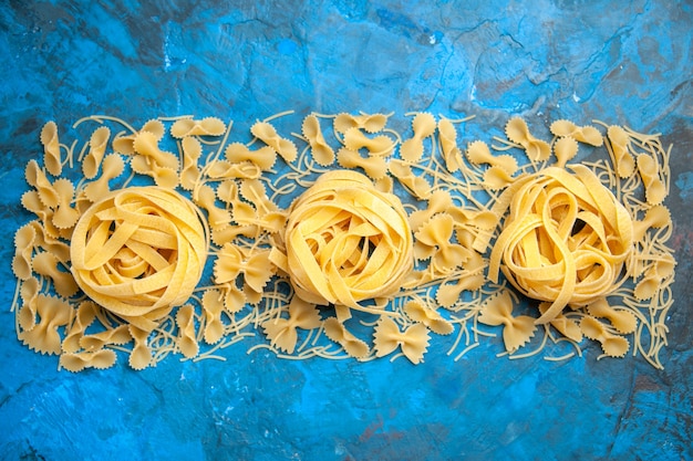 Top view of dinner preparation with pasta noodles lined up in a row on blue background