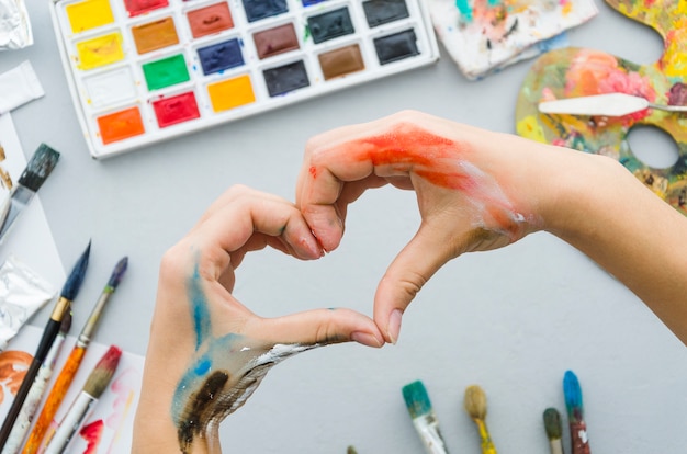 Free photo top view dirty hands making a heart with painting materials