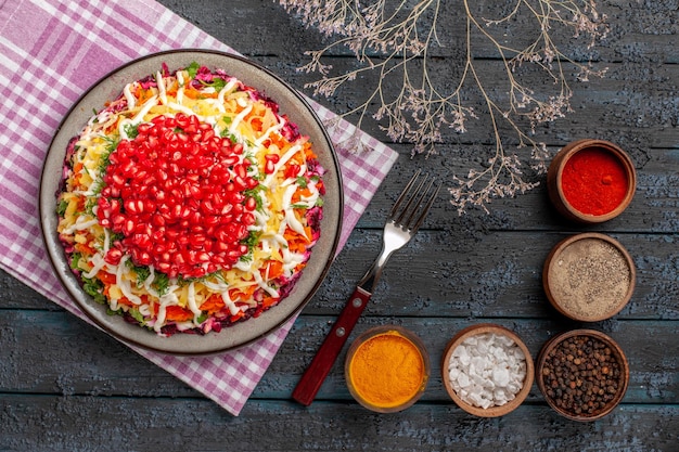 Free photo top view dish and fork appetizing dish on the checkered tablecloth next to the bowls of spices branches and fork on the grey table