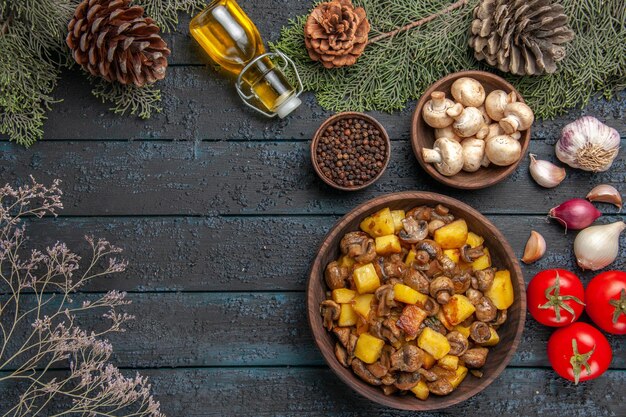 버섯 기름 그릇 아래 버섯과 감자의 상위 뷰 요리와 향신료 접시와 마늘 양파 토마토 옆에 원뿔이 있는 가문비나무 가지