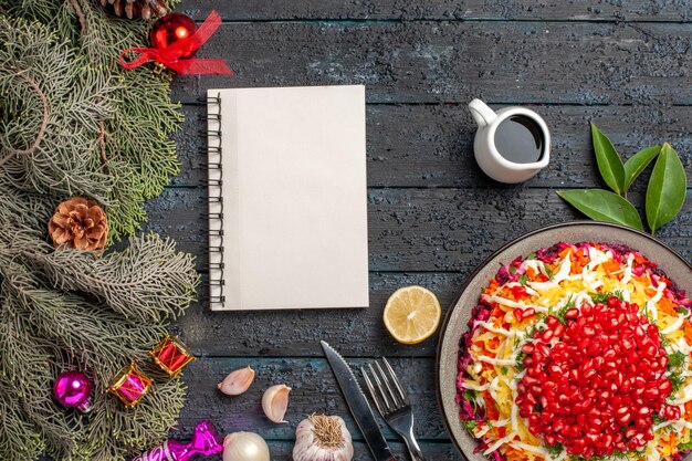 흰색 노트북 포크 나이프 옆에 레몬 마늘 기름 그릇과 콘이 있는 가문비나무 가지와 함께 식욕을 돋우는 크리스마스 요리와 가문비나무 가지