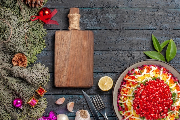 Top view dish and spruce branches appetizing Christmas dish with lemon garlic next to the cutting board fork knife and spruce branches with cones