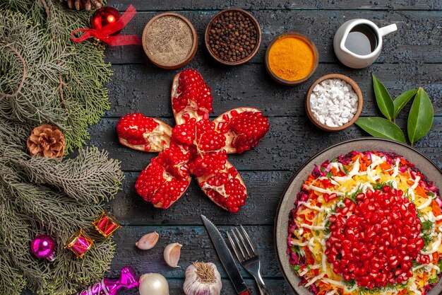 Top view dish and spruce branches appetizing Christmas dish with lemon pilled pomegranate bowl of oil and spices next to the fork knife and spruce branches with cones