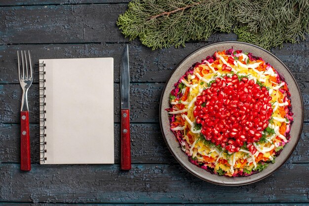 Top view dish and spruce branches Christmas dish next to the fork white notebook knife and spruce branches on the dark table