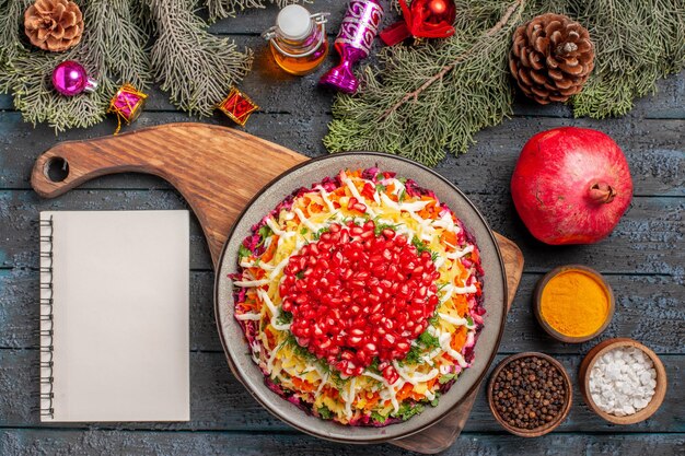 Top view dish with pomegranates dish with seeds of pomegranate next to the white notebook oil spices spruce branches with cones and tree toys