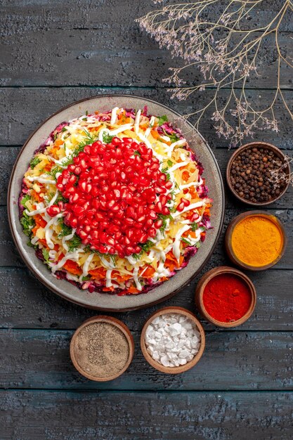 Top view dish with seeds of pomegranate the Christmas dish with seeds of pomegranate next to the bowls of colorful spices and tree branches on the table