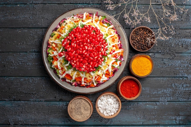 Top view dish with seeds of pomegranate five bowls of spices next to the Christmas dish with seeds of pomegranate and tree branches