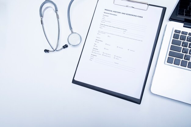 The top view of doctor desktop with stethoscope, clipboard with medical records form and computer laptop