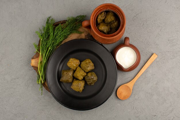 top view dolma green with minced meat inside black plate along with yogurt on the grey floor