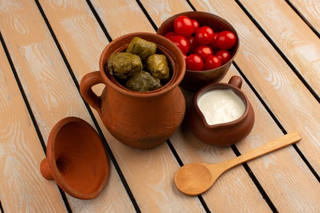 top view dolma in pot along with red tomatoes and yogurt on the wooden floor