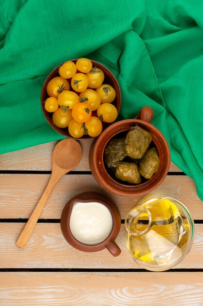 top view dolma with yogurt along with yellow tomatoes and olive oil on the green tissue and wooden rustic floor