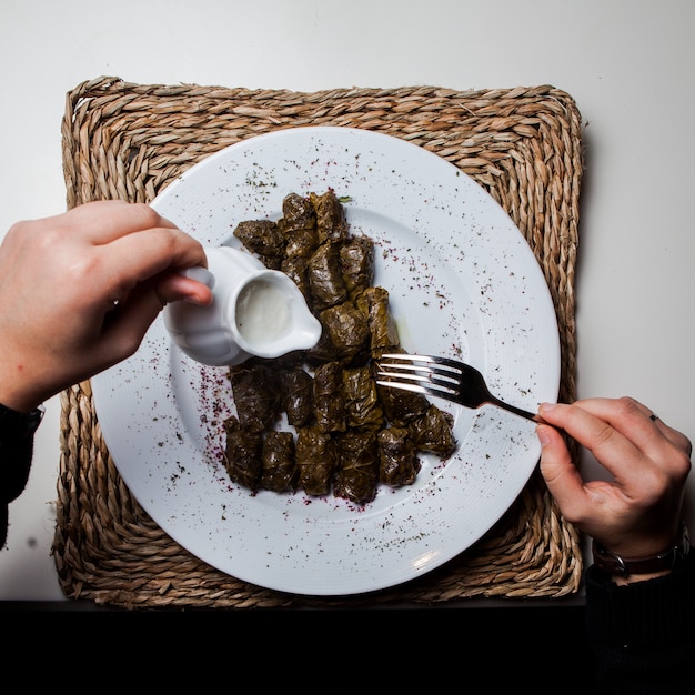 Top view dolma with yogurt and fork and human hand in serving napkins