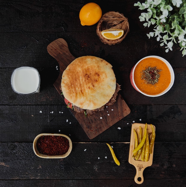 Top view of doner kebab in pita bread on a wooden board served with lintel soup ayran drink and pickled hot green peppers on the wooden wall