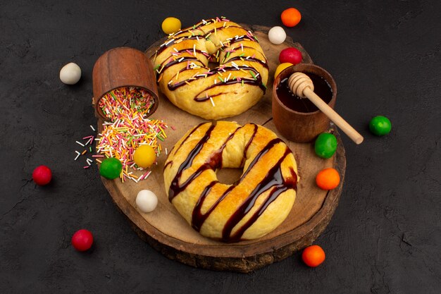 Free photo top view donuts sweet yummy delicious choco lined along with multicolored candies on the brown desk and dark