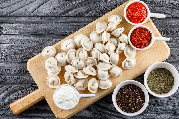 Top view dough on a cutting board with sauce, spices in bowls on gray wooden surface. horizontal