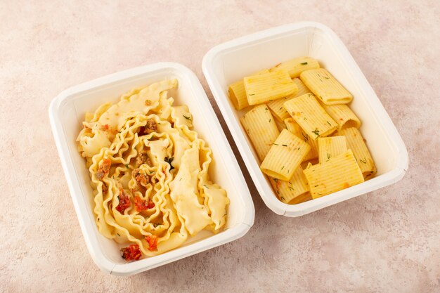 A top view dough meal and italian pasta with tomatoes and meat inside white bowls on pink