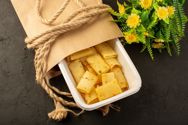 Foto gratuita un pasto della pasta di vista superiore con le erbe verdi essiccate all'interno della ciotola e del pacchetto bianchi insieme al fiore sull'oscurità