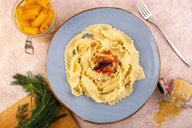 A top view dough pasta cooked tasty salted inside round blue plate with flower and raw pasta on pink desk