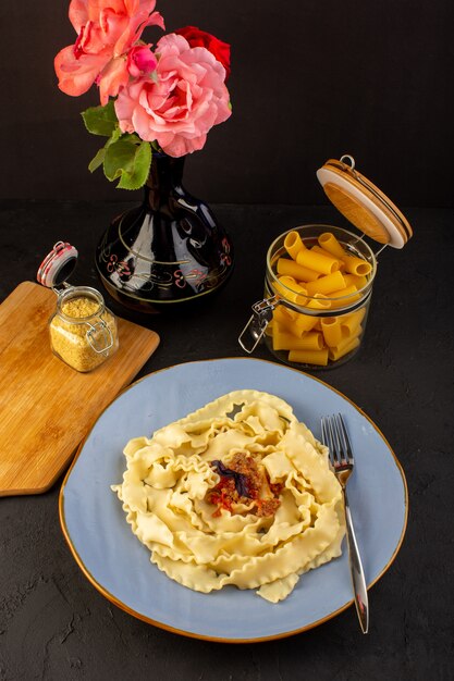 상위 뷰 반죽 파스타는 디자인 된 카펫과 어두운 책상 이탈리아 식사 요리에 용기 안에 와인과 꽃 잔과 함께 둥근 파란색 접시 안에 맛있는 소금에 절인 요리