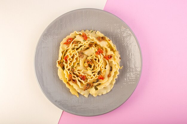 A top view dough pasta with cooked meat and vegetables inside grey plate on white-pink