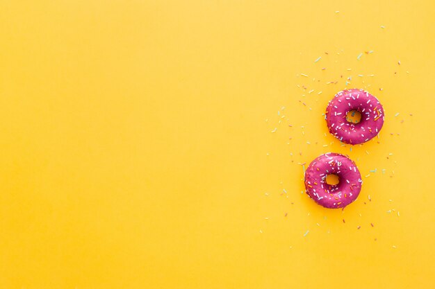黄色の背景にピンクのアイシングでドーナツのトップビュー