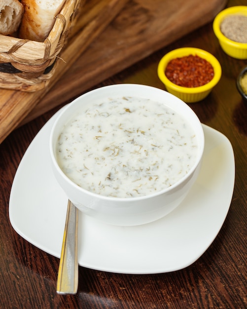 A top view dovga with greens inside white plate on the brown wooden desk food soup yogurt meal