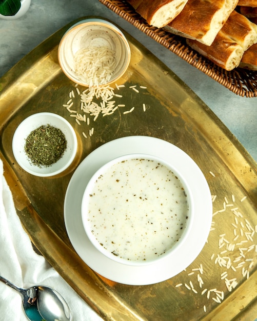 Top view dovga-yogurt soup traditional azerbaijani soup with rice and dried herbs on a tray