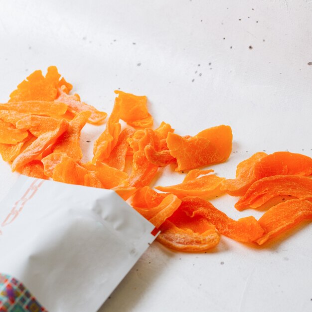 A top view dried apricot pieces inside and outside little paper package on white