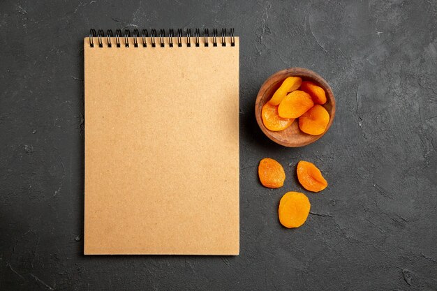 Top view dried apricot raisins with notepad on dark surface dry fruit raisin