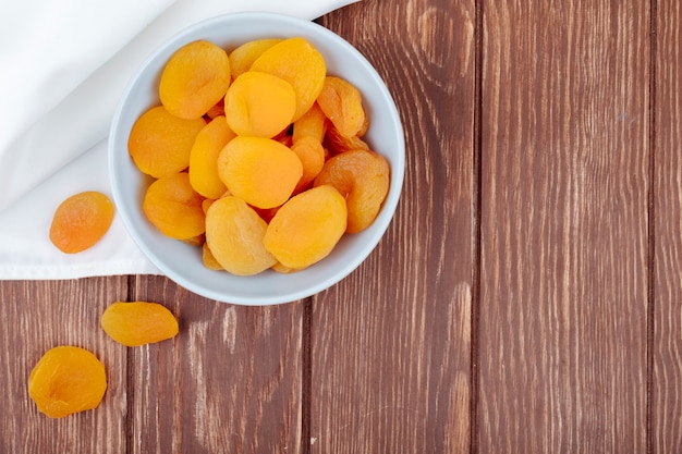 Top view of dried apricots in a white bowl on wooden background with copy space